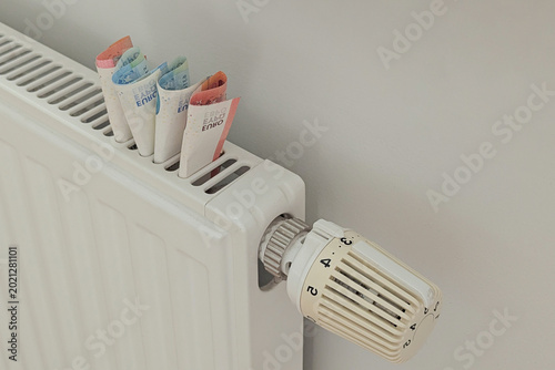 Fotografie Closeup euros tucked in radiator near thermostat, symbol of rising heating costs