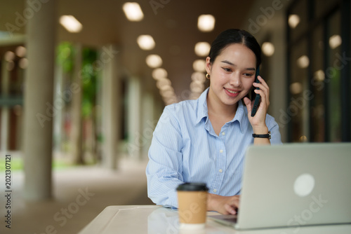 Foto Young Asian businesswoman multitasking, having a phone call while typing on a la