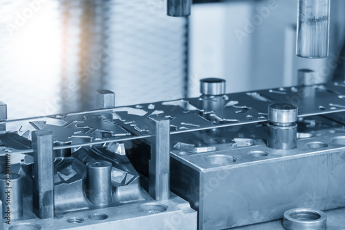 Fotografie Industrial operation of a progressive die forming high-precision sheet metal parts in a blue-toned scene with lighting effects