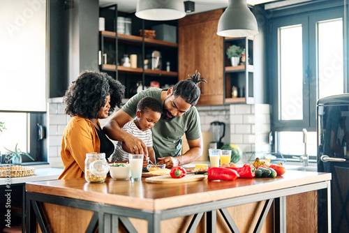 Portrait of mother, father and son preparing and eating breakfast in the kitchen at home