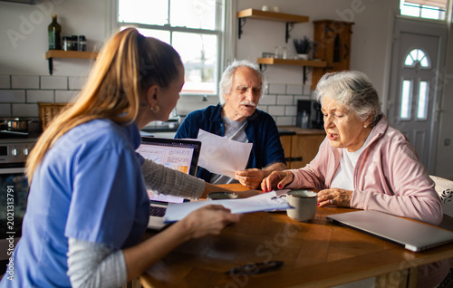 Home nurse helps senior couple review medical paperwork at kitchen table