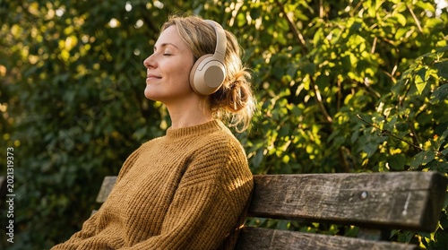 Peaceful woman sitting on a park bench wearing wireless headphones and listening to music with her eyes closed.