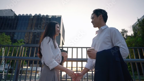Young Asian business professionals having conversation outside office building while holding coffee cup and tablet device. Modern teamwork and collaboration in urban workplace.
