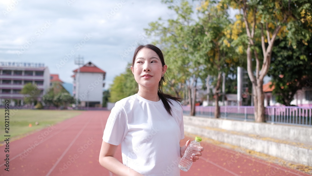 Fototapeta premium Female athlete taking a break outdoors, drinking water, with water bottom, Happy sportswoman taking a water break outdoors