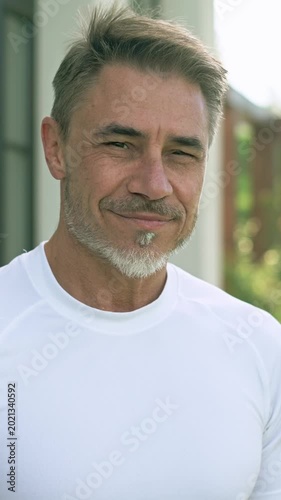 Portrait of relaxed middle-aged man smiling enjoying garden on sunny day. Happy handsome male in 50s with gray hair and beard on terrace at home.