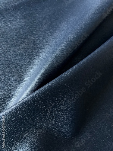 Dark navy blue leather texture with elegant folds and fine grain detail, featuring premium luxury material, smooth abstract surface and modern minimalist aesthetic in close-up composition.