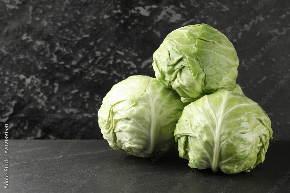 Fototapeta premium Fresh cabbages on black textured table, closeup. Space for text