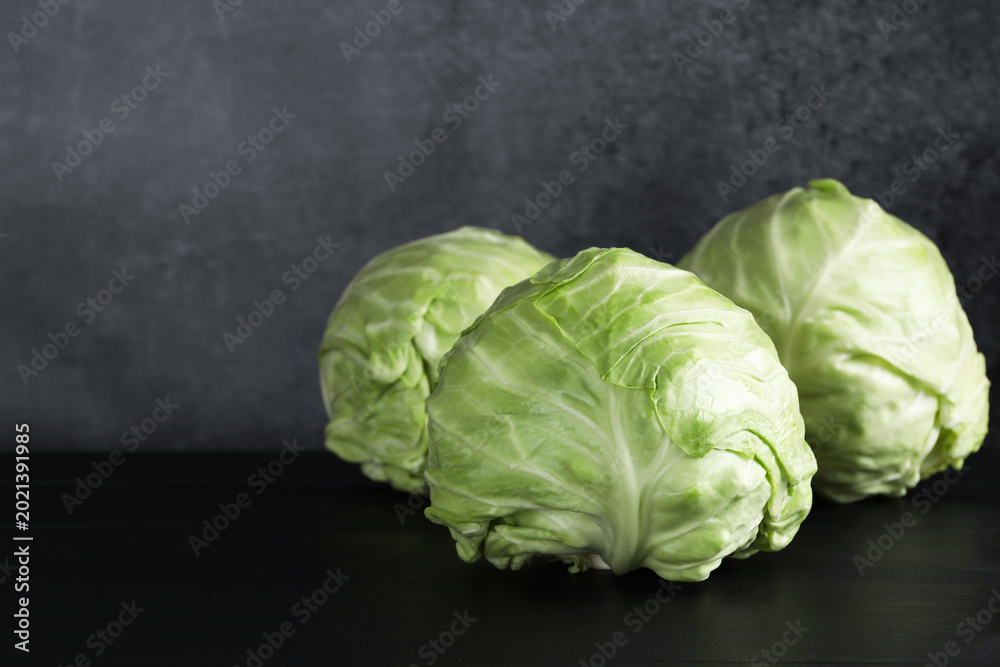 Fototapeta premium Fresh ripe cabbages on black wooden table, closeup. Space for text