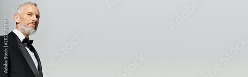 Foto Elegant middle aged man in a black tuxedo posed gracefully in a grey studio sett