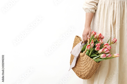 Woman holding wicker bag with beautiful tulips and handkerchief on light back...