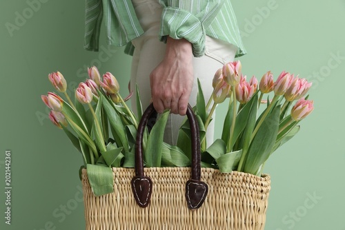 Woman holding wicker bag with beautiful tulips on green background, closeup