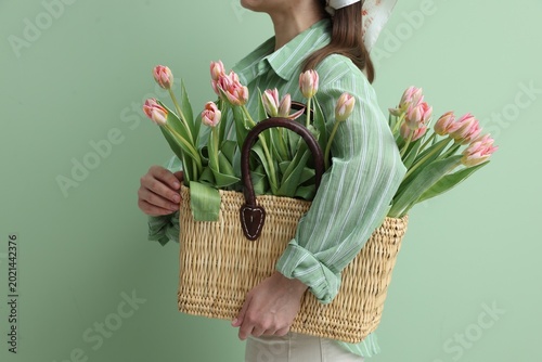 Woman holding wicker bag with beautiful tulips on green background, closeup