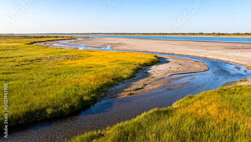 A winding water channel flows through a grassy wetland landscape under a clear blue sky