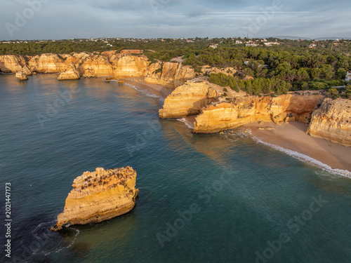 Drone view of Praia da Marinha beach in Algarve, Portugal, with golden cliffs, an offshore rock, turquoise Atlantic water, and a sandy cove.