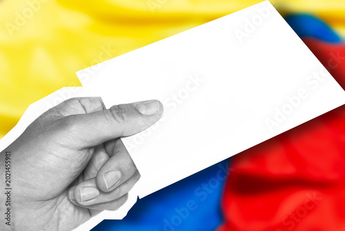 Hand holding a blank paper in front of a blurred Colombian flag, representation of citizen participation, voting, and the Colombian democratic context. Template with copy space