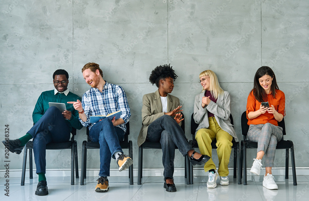 Fototapeta premium Group of young businss people sitting in chairs and waiting for an interview holding application documents