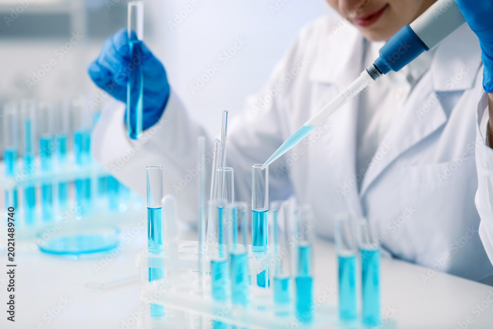 Fototapeta premium Scientist dripping blue liquid into test tube at white table in laboratory, closeup
