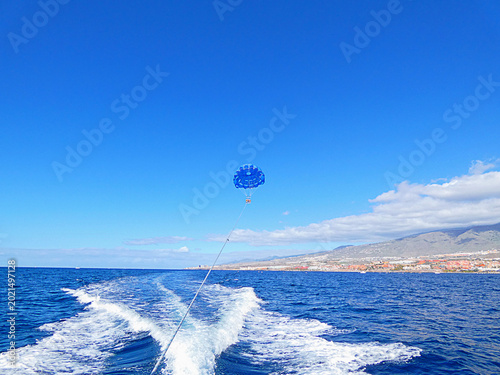 Принти на полотні Blue parasail flying above Atlantic Ocean behind speeding boat near Tenerife coastline and mountain landscape