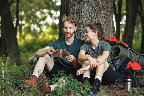 Photo of couple sitting in forest at summer with backpacks