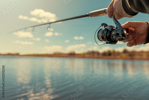 A fishing rod with a spinning reel in the hands of a fisherman on a spring day. Fishing background.
