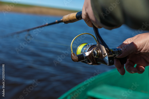 A fishing rod with a spinning reel in the hands of a fisherman on a spring day. Fishing background.