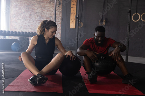 Diverse training partners sitting on red mats gripping 14 LB medicine ball in gym