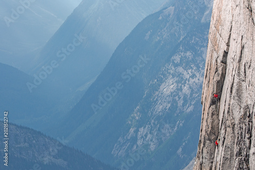 Two climbers high on a steep wall looking over a beautiful valley.
