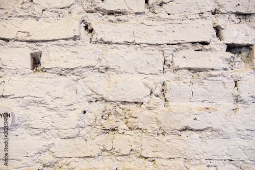 Close-up, straight-on view of an old brick wall, painted unevenly with white paint. 
