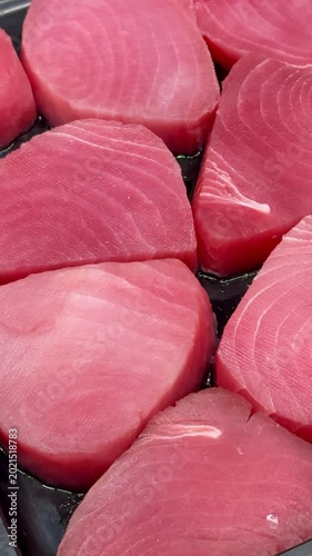 Pink tuna steaks on black tray, supermarket shelf closeup, chilled display of raw fresh fillets arranged in neat rows, subtle