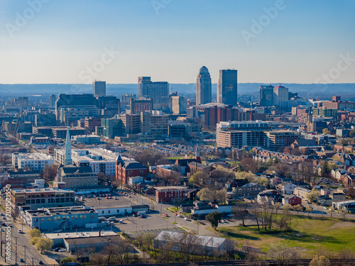 Aerial view of the Louisville skyline featuring modern skyscrapers, historic brick buildings, and urban streets under a clear blue sky in Louisville, Kentucky, United States.
