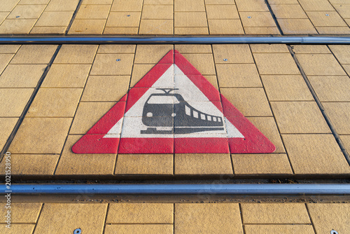 A traffic sign warning of a railway crossing, painted between the train tracks. The sign is intended to indicate that trams or trains travel along this route. 