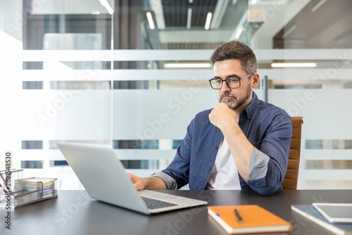 Картината върху платно Confident businessman in a modern office concentrates on his laptop, analyzing s