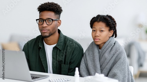 Young adults bundled under blanket with laptop indoors