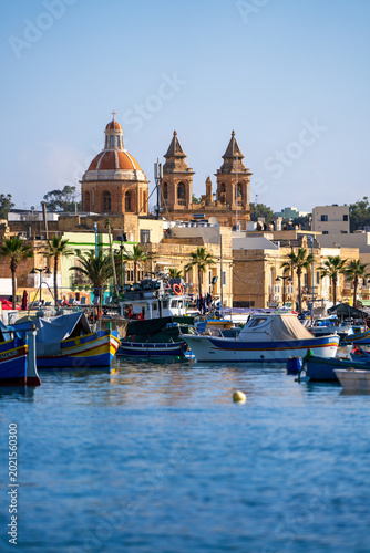 Schilderij op canvas Vertical View of Marsaxlokk Harbor with Traditional Fishing Boats and Parish Chu