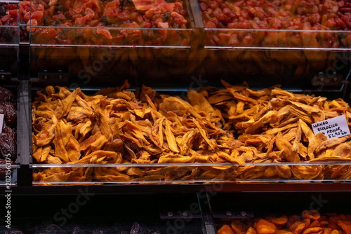 Quadro su tela Eye-level shot of orange dried mango strips stored in a professional glass partition at a market, featuring dates and other dried fruits in the periphery