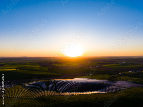 Sunrise over solar panels in a rural area with fields and hills in the background capturing the early morning light and changing colors of the sky