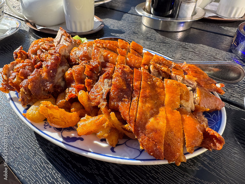 Crispy pork knuckle with onion rings on blue and white plate