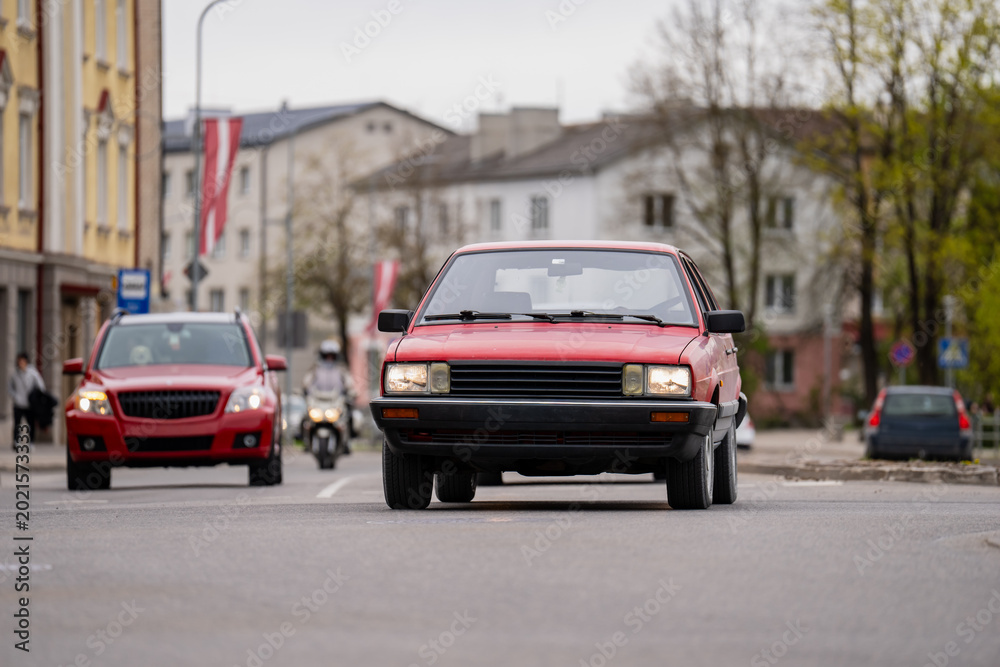 Fototapeta premium Classic red vehicle with headlights on traveling through a European town street illustrating automotive history and daily urban mobility within a metropolitan environment