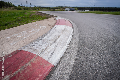 Obraz na plátně Curving asphalt road of a racing circuit featuring weathered red and white rumbl