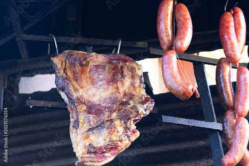 Savory beef ribs and plump sausages slow-cooking on a rustic metal grill. 
