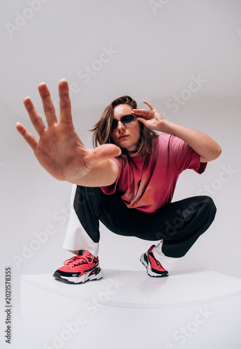 Emotional female hip hop dancer posing and dancing on a gray studio background. Dynamic wide-angle shot with joy, laughter, and urban street style