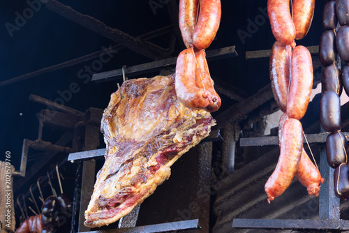 Rustic beef and various sausages slow cooking on a metal smoker. 