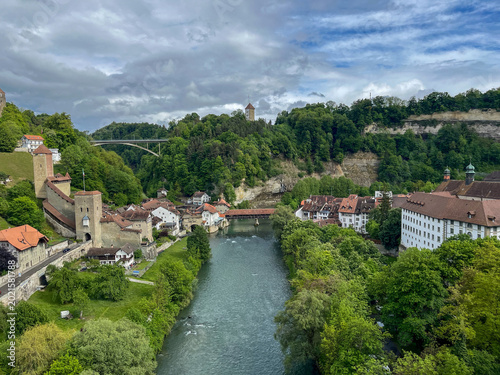 Scenic view of the Sarine river winding through the historic old town of Fribourg, Switzerland under a dramatic sky.