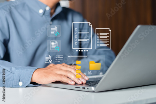 Businessman using laptop with digital document management system and cloud storage icons. Paperless office transitions, electronic document filing, data organization, and cloud accessibility