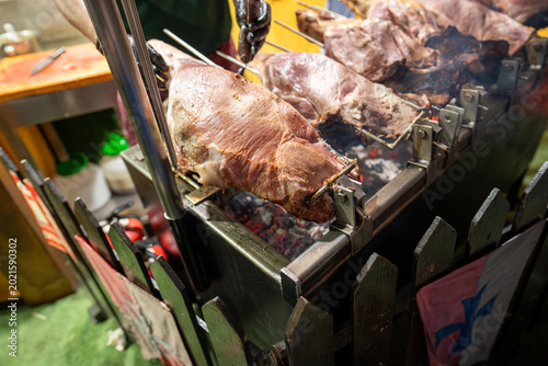Fotografia Close-up of a large leg of meat rotating on a spit above a bed of hot coals, showing the searing process and rendered fat