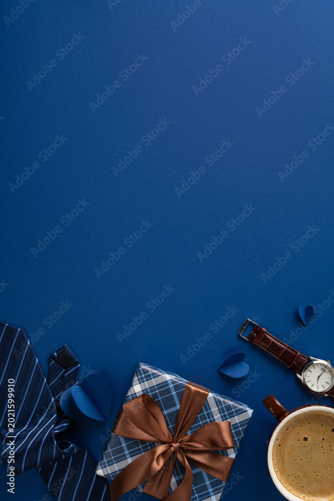 Fototapeta premium Blue Father's Day vertical flatlay with wrapped gift, tie, watch, coffee and brown ribbon bow