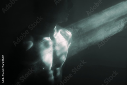 Dramatic male torso illuminated by a directional beam of light with textured highlights for moody background and poster design