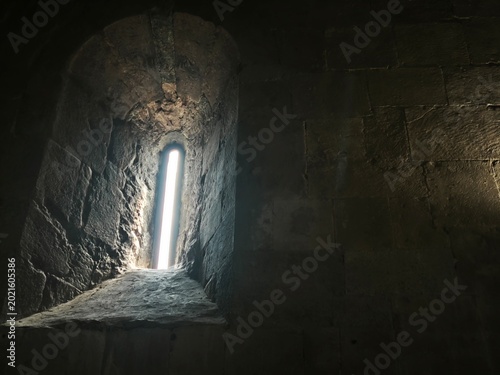 Φωτογραφία Bright light streaming through a narrow arched window in a dark stone wall