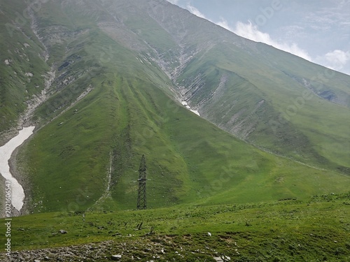 Valokuva Massive steep green mountain slope with deep ravines and snow patches