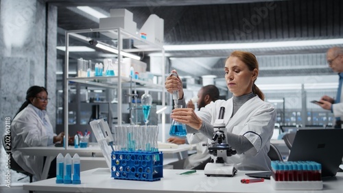 Schilderij op canvas Female researcher in lab pipetting blue liquid into test tube to analyze it